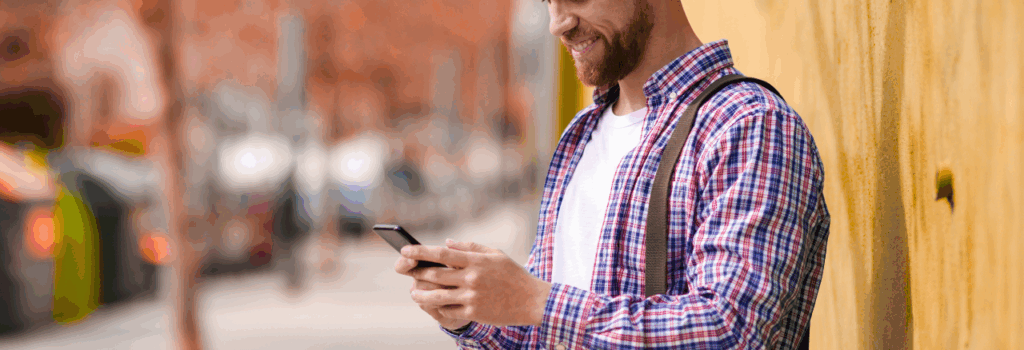 man standing near yellow building look down at mobile phone after parking on street near building