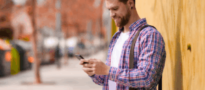 man standing near yellow building look down at mobile phone after parking on street near building
